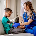 Healthcare professional checking blood pressure of young child during mobile virtual urgent care visit at home