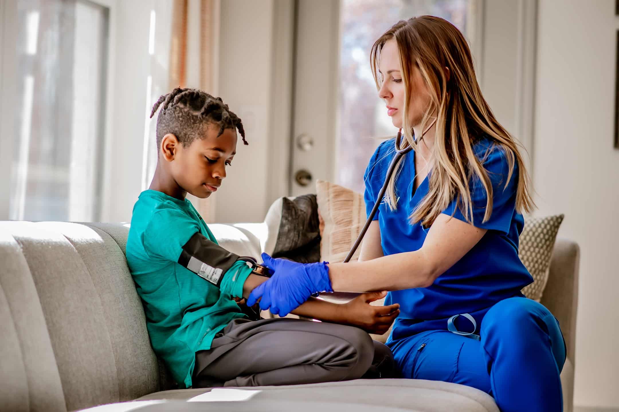 Healthcare professional checking blood pressure of young child during mobile virtual urgent care visit at home